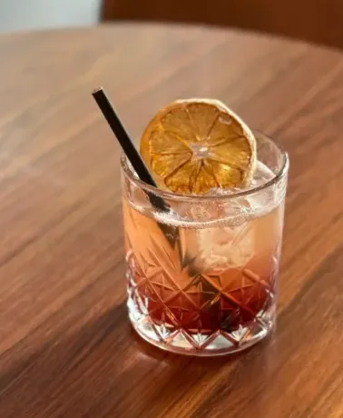 Cocktail ambré sur glace, garni d'orange, sur une table en bois