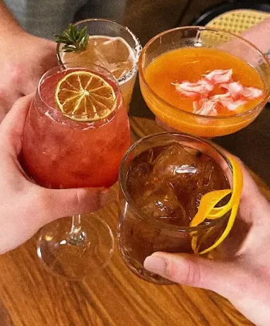 Quatre cocktails qui trinquent au-dessus d'une table en bois